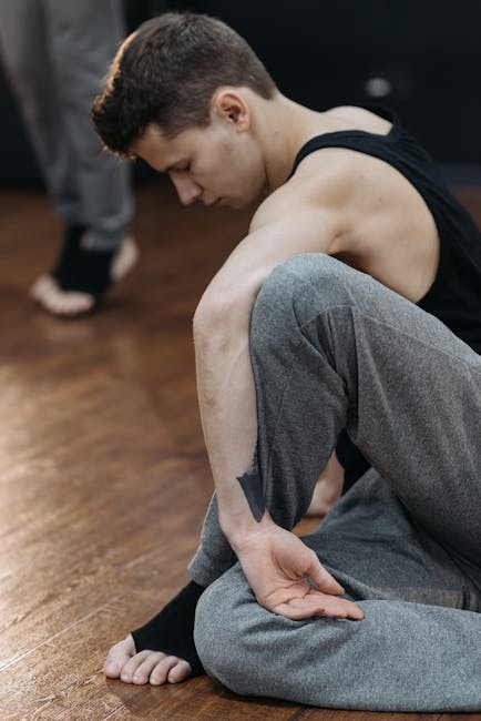 Smiling man in athletic clothes sitting on a yoga mat and stretching his legs.